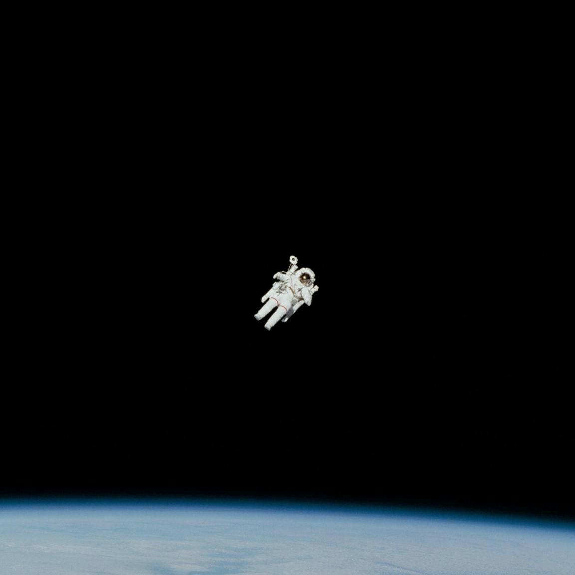 An astronaut floating in space with a black background and a sliver of the earth in the bottom of the frame