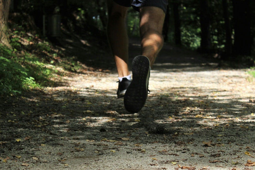 Photo of person's lower body as they jog along a sandy trail.