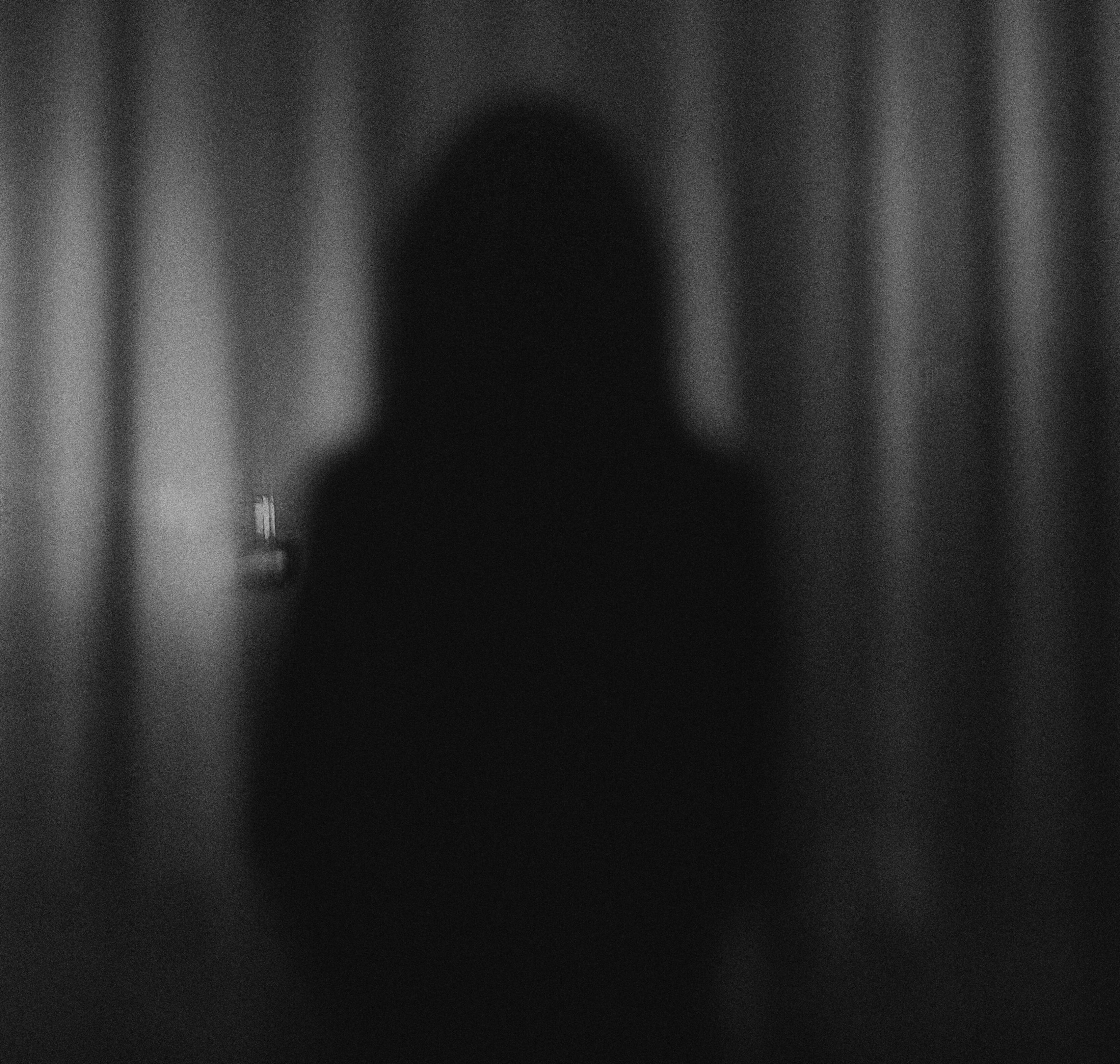 Photo of out-of-focus person standing near a curtain-covered window.